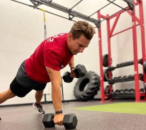 fitness trainerdoing push ups with dumbbell row in functional training room